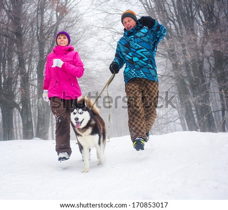 Beautiful girl and boy walking with husky dog in winter forest