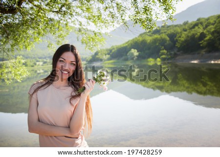 Beautiful woman with flowers in hand near mountain lake