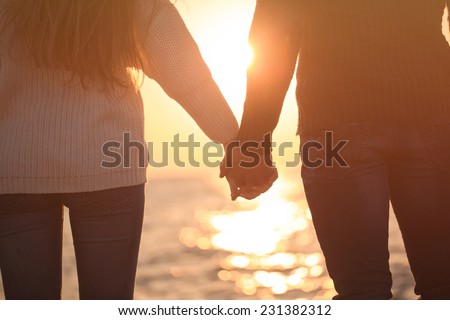 Two lovers holding their hands on the shore of the sea