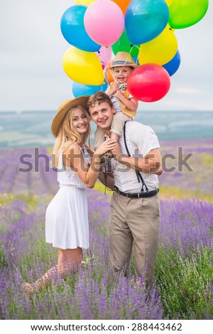 Happy young family of three person walking on lavender field with color balloons