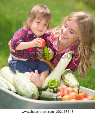 mom and son with vegetables harvest in garden. little boy sitting in the wheelbarrow