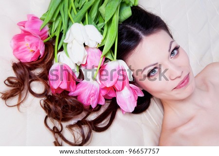 Beautiful brunette girl laying in bed with tulip flowers