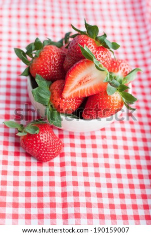 Small bowl filled with succulent juicy fresh ripe red strawberries on table with red checkered tablecloth