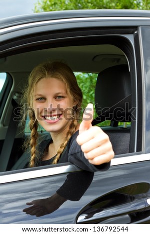 Smiling  young woman drive a car and looking at camera with thumb up