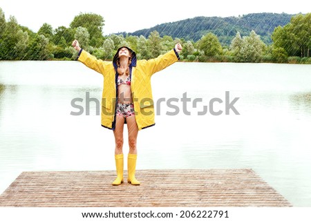 Happy girl in a yellow rain coat and bikini enjoy a rain shower