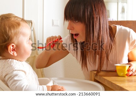 Young mother feeding girl baby in high chair