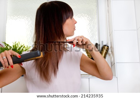 Young woman in bathroom with hair straightener
