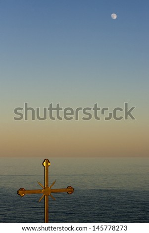 Golden cross, full moon and quiet sea at twilight.