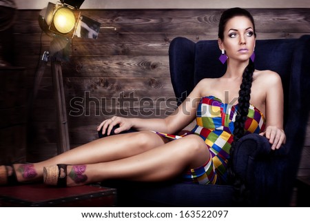 Nice beautiful brunette with braided long hair is sitting in dark blue chair looking left
