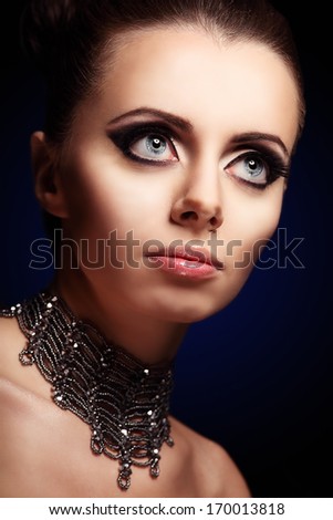 Gothic beautiful woman with giant pretty blue eyes and evening makeup on black background looking up to the right side