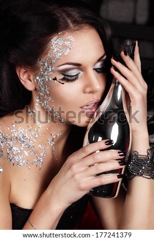 Attractive woman with silver makeup is having a party and touching the bottle of champagne with her pink lips