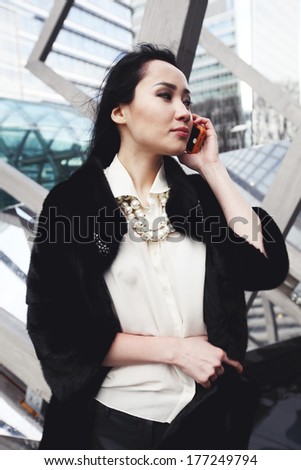 Beautiful asian business woman in London standing on the street in the city and talking by the mobile phone