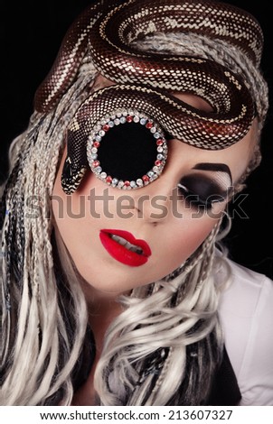 Young female portrait with californian king snake on her face over the goggle monocle full of colorful rhinestones