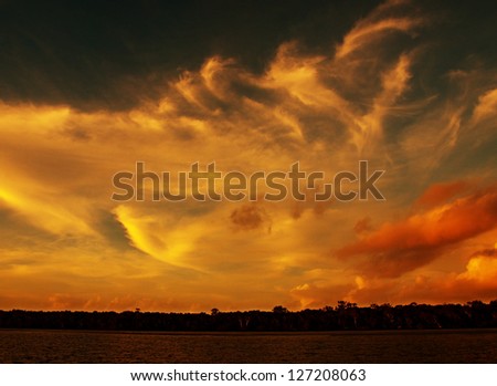 Multicolored, gold, orange,white and black turbulent wispy sunset over water and through cloud ( colorful background ) .
