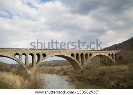 Old stone middle age bridge in Bulgaria, against a cloudy sky