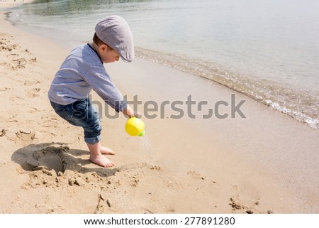 Cute little boy playing with watering can on the beach