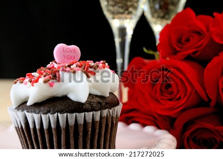 Valentine\'s day cupcake with love you candy heart, red roses, and champagne.
