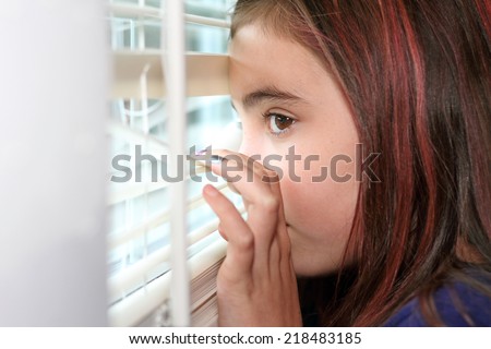 Brown eyed eleven year old girl peeking out window.