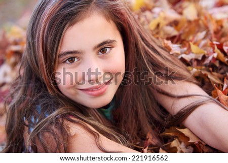Portrait of eleven year old girl smiling in leaf pile.