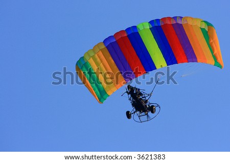 a person flying a powered parachute through the blue sky