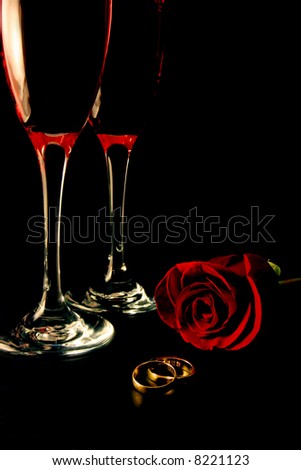  glasses with rose and wedding band rings over black background ready for