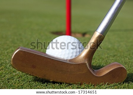 Golf putter lined up with ball on green.