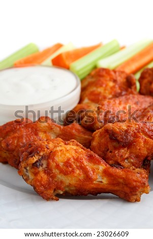 Buffalo chicken wings on plate with blue cheese sauce, carrots, and celery.