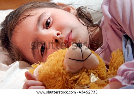 Sad child crying in bed and hugging teddy bear