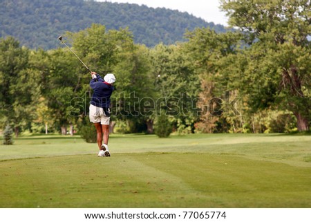 African american woman driving golf ball down golf course fairway.