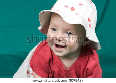 Baby in fish print hat smiling on green background