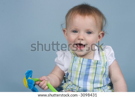 Baby holding toy flower smiling on a blue background