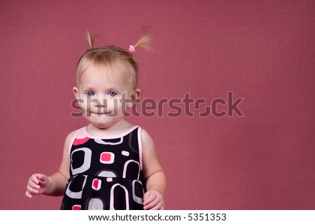 A cute baby dressed in a retro dress with pig tails on a pink background