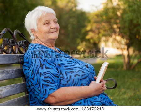 Senior woman reads the book sitting on a bench