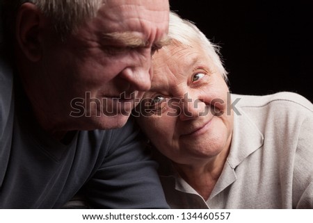 A loving, handsome senior couple on a black background.