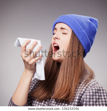 Sick young woman with a flu, sneezing closeup  over grey