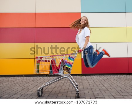 The happy girl the teenager joyfully jumps near to the cart full of purchases