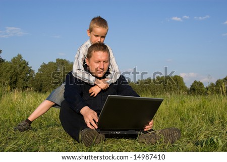 The daddy and the son play the laptop on a green grass