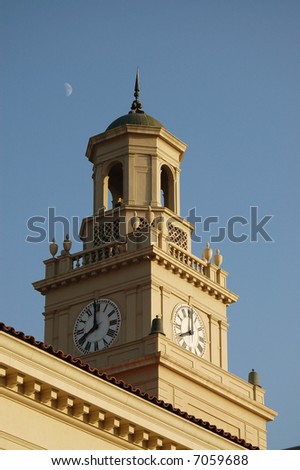 Chapel clock and bell tower side lit by setting sun with the moon in the late afternoon sky; University of Redlands; Redlands, California