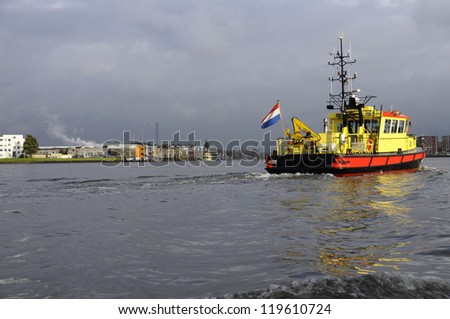 Red and yellow trawler with Nederland flag in Amsterdam harbor on a rainy day