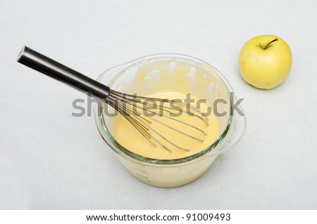 Pate for apple cake in a glass bowl and whisk, with an golden apple next
