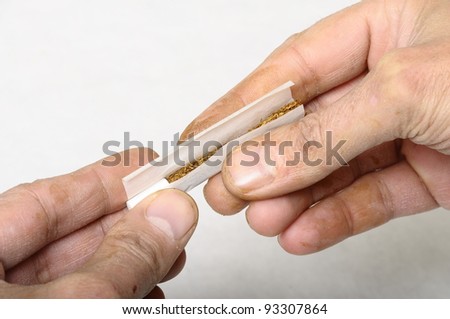 Hand of manual worker (with spots of  paint and varnish) rolling a cigarette with rolling tobacco on clear background