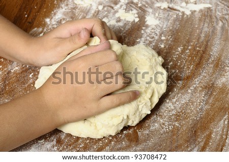 Child\'s hands kneading bread dough on wooden table with flour