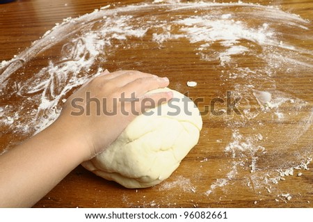 Child\'s hands kneading bread dough on wooden table with flour
