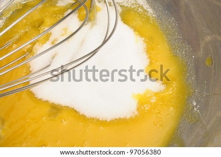 Some sugar poured on egg yolk and whisk ready to mix