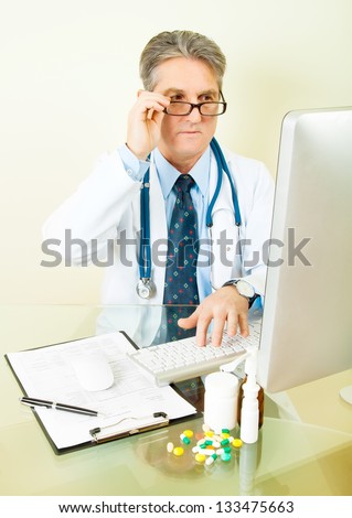 Smiling Doctor on his workplace with computer, pills, tablets, and patient data history