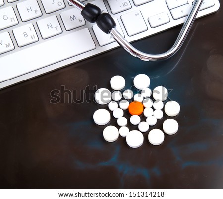 different - one red, orange pill among white pills on x-ray, near keyboard and stethoscope