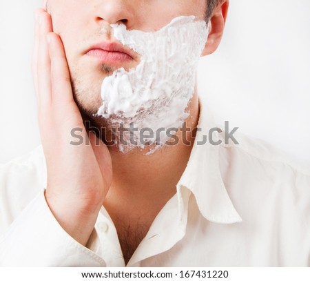 Young man with foam shaving his beard off with an electric shaver