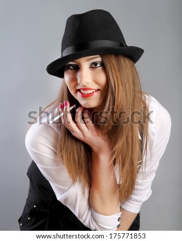 beautiful young woman in hat smoking cigarette in studio grey background