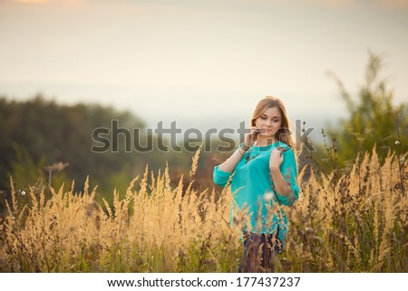 Young pretty woman with long hair standing on a field with sunrise on the background