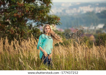 Young pretty woman with long hair standing on a field with sunrise on the background